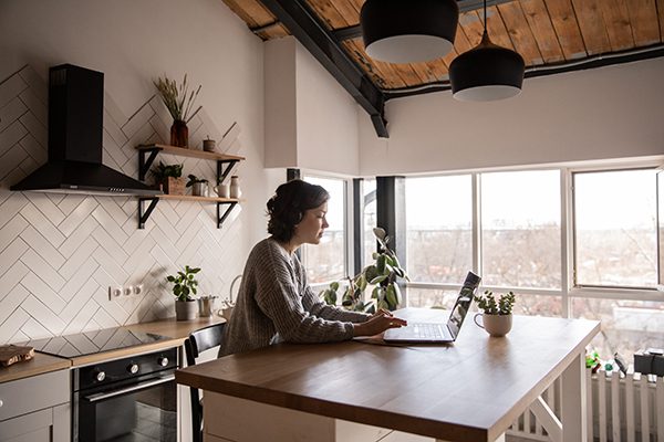 A woman works at a laptop in the kitchen